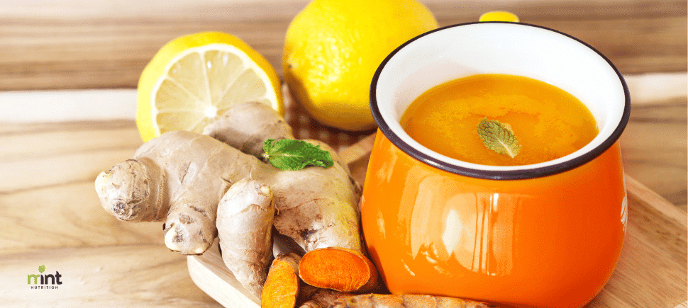 Photo of a lemon ginger detox drink in an orange mug on a wooden table surrounded by lemons and fresh ginger