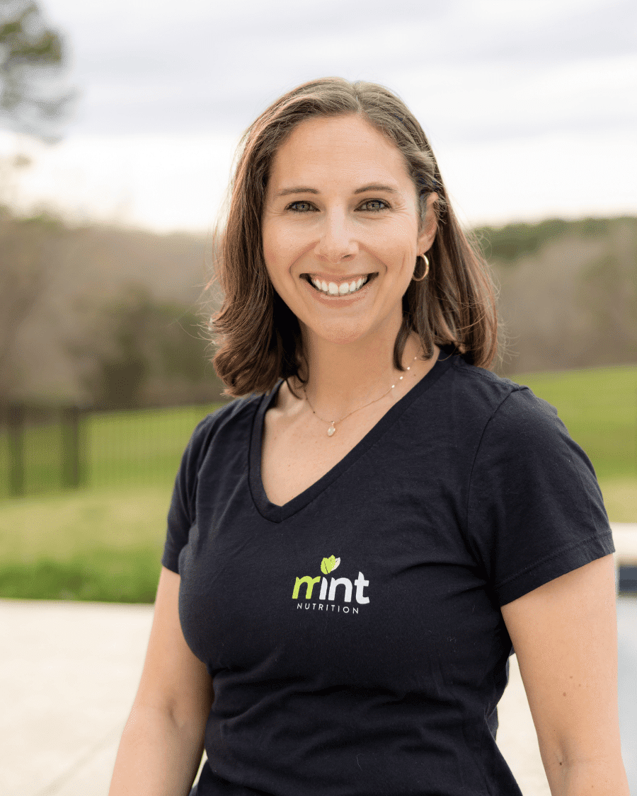 A photo of MINT Nutrition registered dietitian, Brynn. She is smiling and wearing a black v-neck shirt with the MINT Nutrition logo.