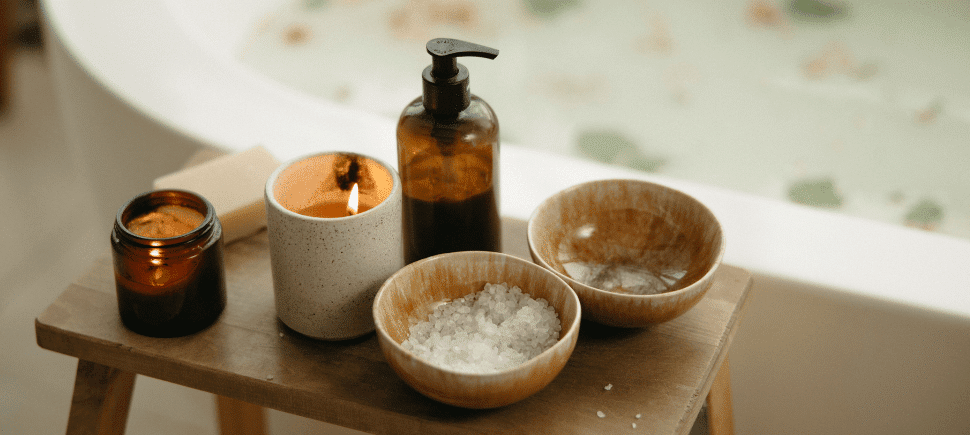 Photo of a calming ritual to relieve stress, recommended by a Mooresville, NC dietitian — a filled tub for a warm, relaxing bath. There are Epsom salts, lotion, and lit candles on a small wooden table nearby.