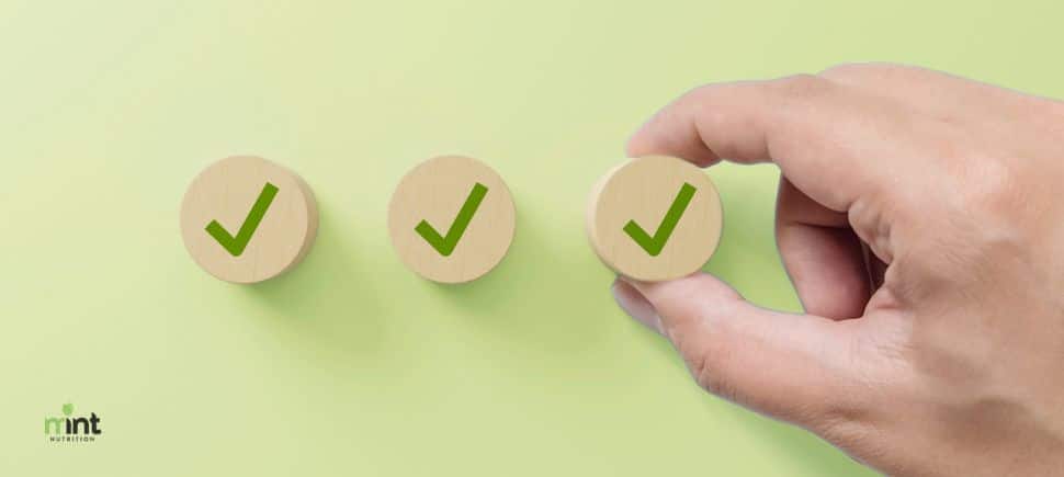 Hand placing a checkmark, representing the CIRS symptom checklist used to spot chronic inflammatory response syndrome. MINT Nutrition logo in bottom left corner.