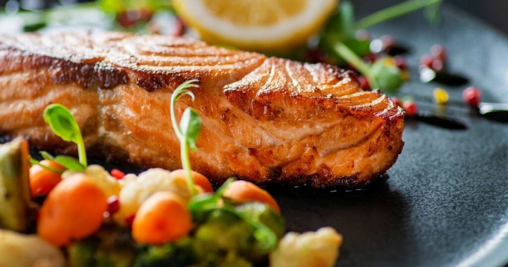 Seared salmon fillet with roasted vegetables and lemon, a protein-rich meal that supports muscle and autophagy